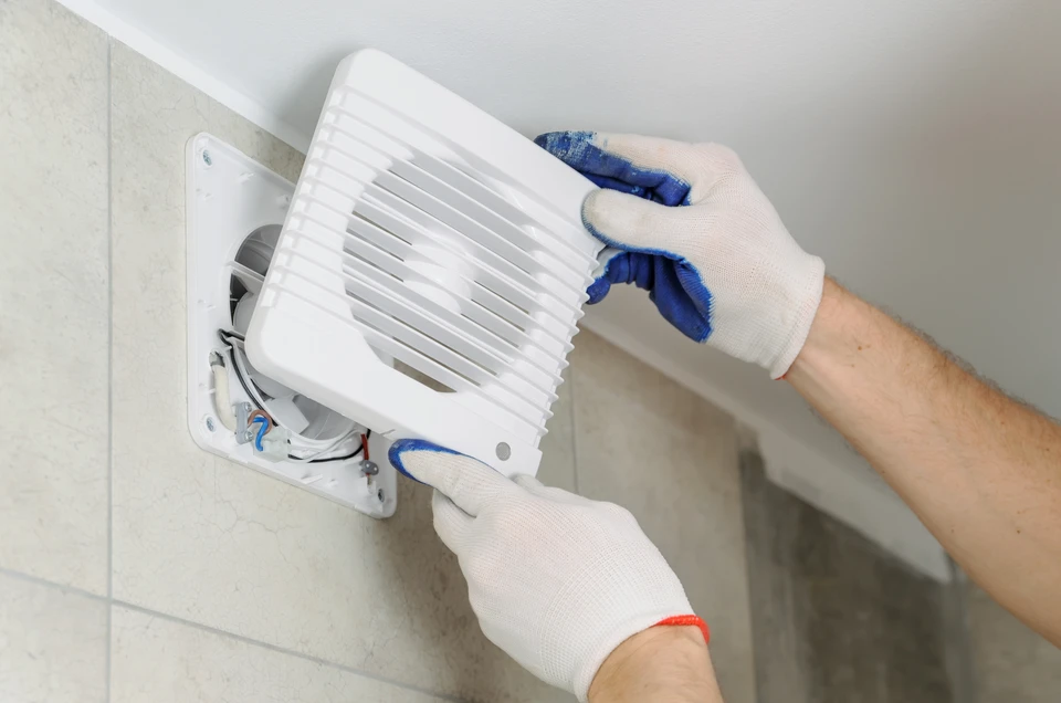 Intérieur de salle de bain, technicien en gants blancs installant ou réparant un ventilateur d'extraction murale