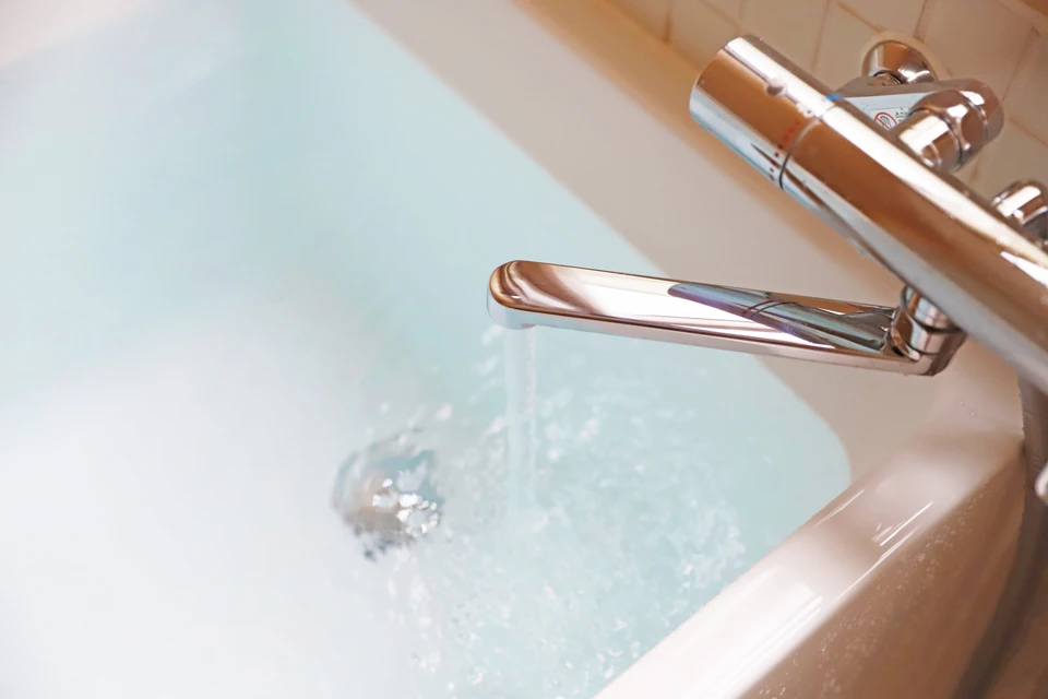 Scène intérieure de salle de bain avec robinetterie chromée moderne en fonctionnement, eau coulant dans baignoire blanche