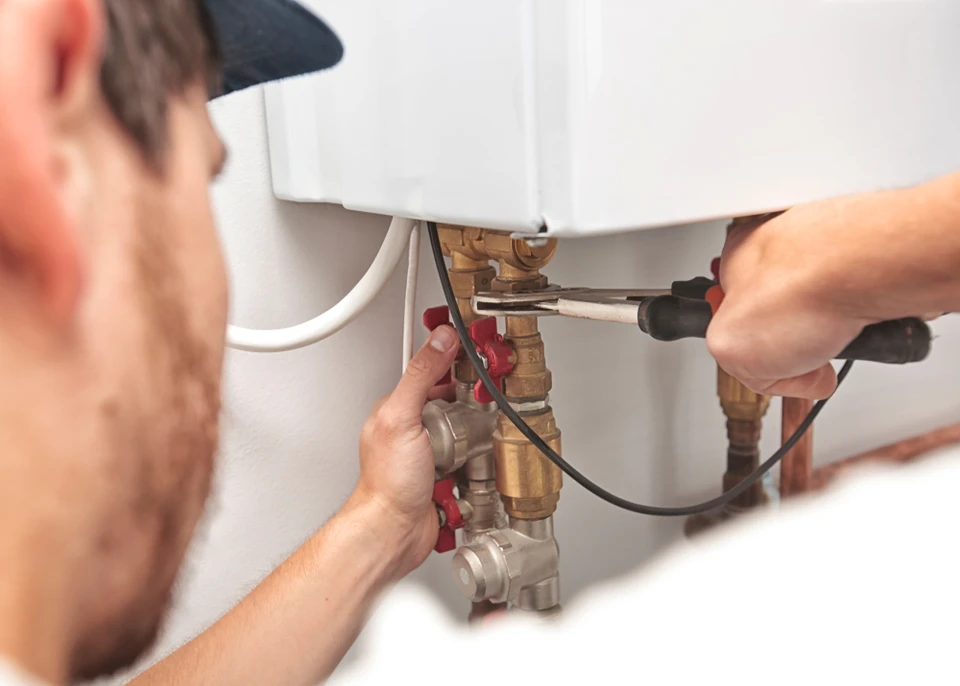 Plombier professionnel intervenant sur chauffe-eau domestique, utilisant un multimètre pour diagnostic électrique