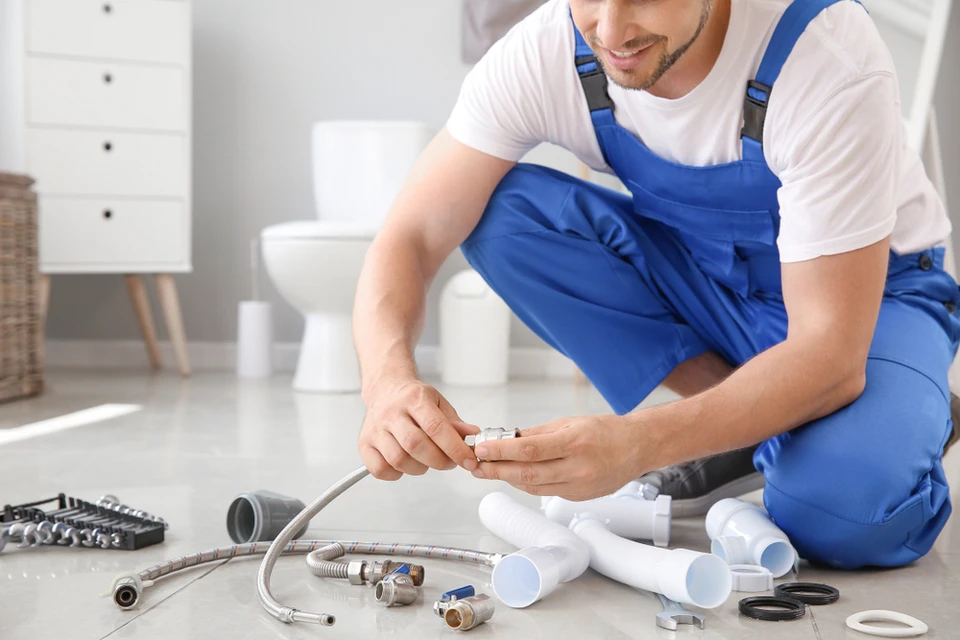 Plombier en salopette bleue travaillant à genoux dans salle de bain moderne, manipulant outils de plomberie