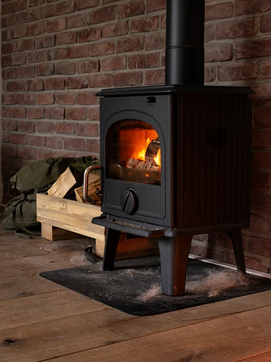 Flammes orange et jaunes s'élèvent d'un lit de granulés de bois cylindriques en combustion, avec arrière-plan de briques réfractaires