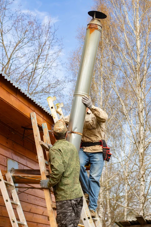 Technicien en combinaison bleue et casquette installant un radiateur mural blanc dans une pièce aux murs blancs et parquet clair