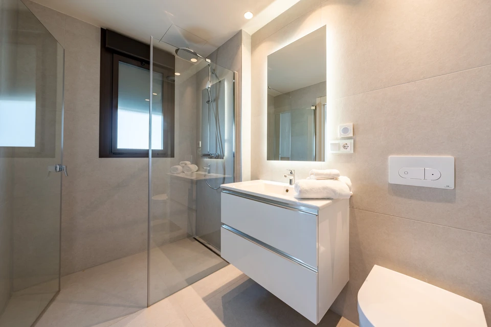 Salle de bain moderne minimaliste avec douche à l'italienne vitrée, meuble vasque suspendu blanc à tiroirs, miroir éclairé par spots LED